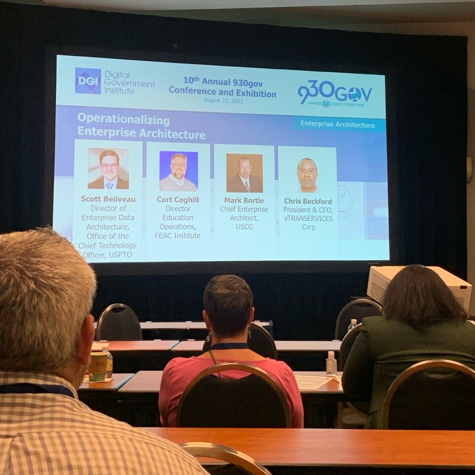 Conference session at the 10th Annual 930gov Conference and Exhibition on August 23, 2022. The presentation, titled 'Operationalizing Enterprise Architecture,' features panelists including Scott Beliveau, Cort Coghill, Mark Bortle, and Chris Beckford, with attendees seated in the foreground.