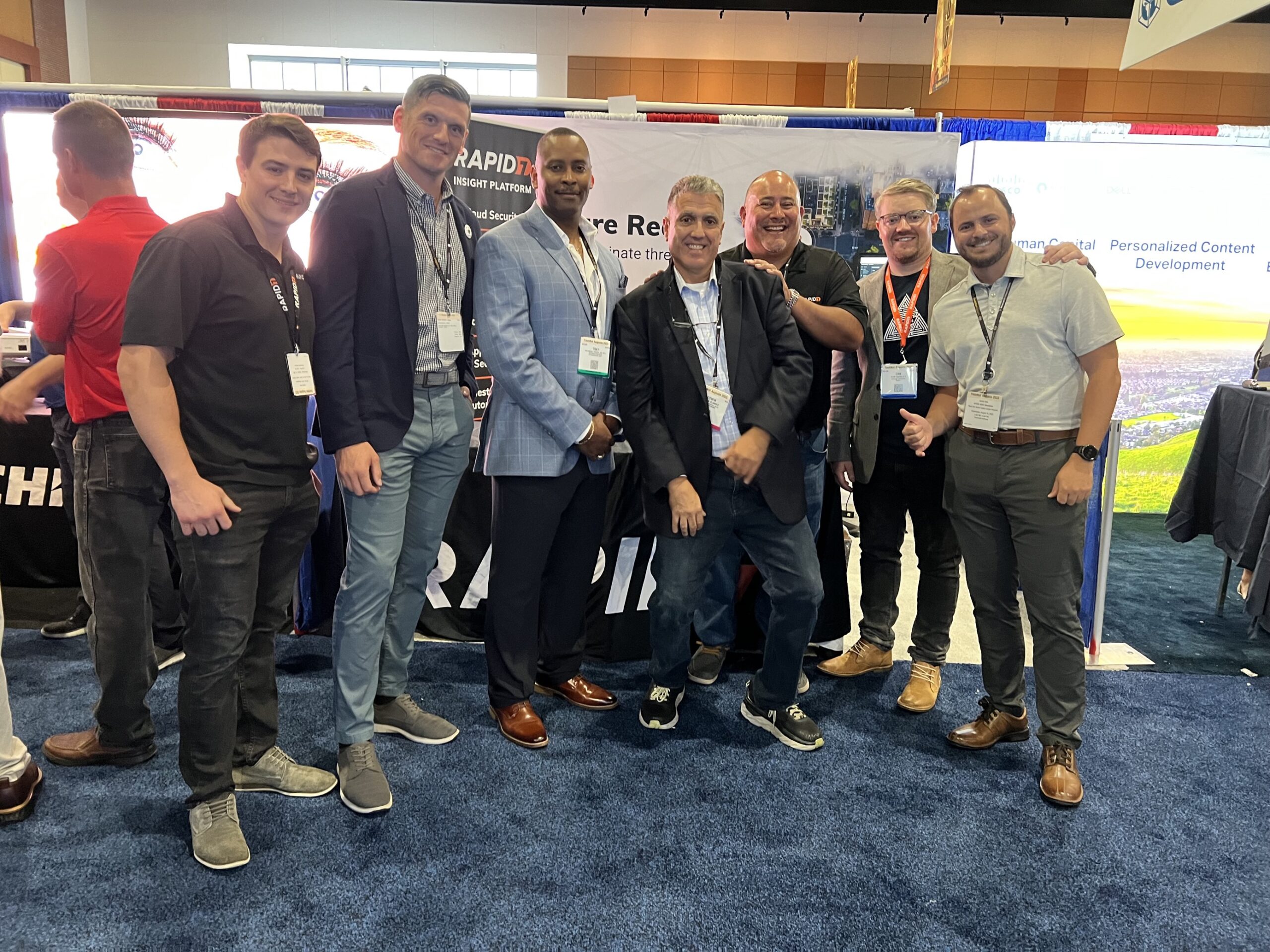 Seven men posing together in front of a booth during an event