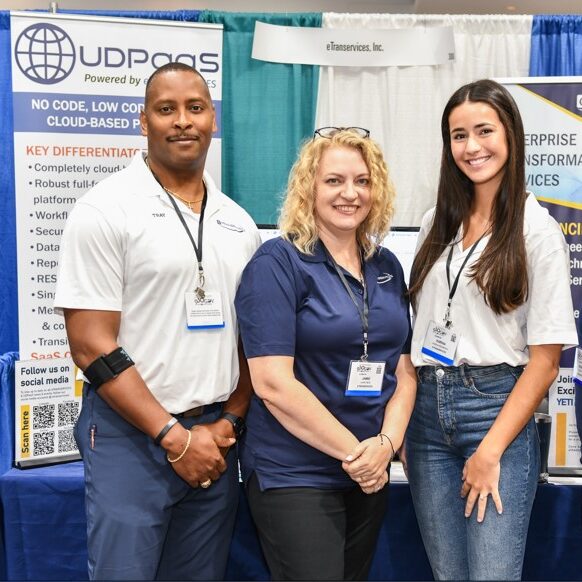 One man and two women posing for a photo in front of a booth during an expo event