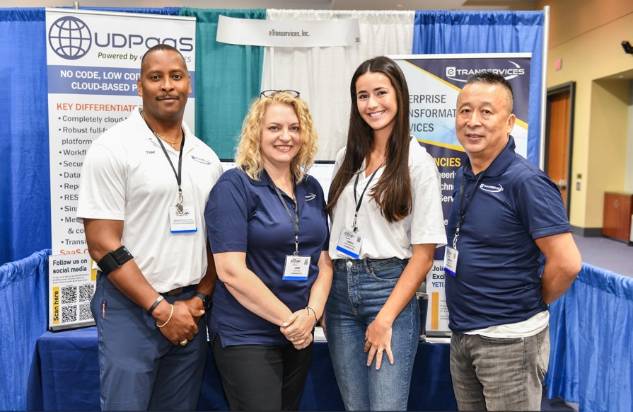 Two men and two women posing for a photo in front of a booth during an expo event