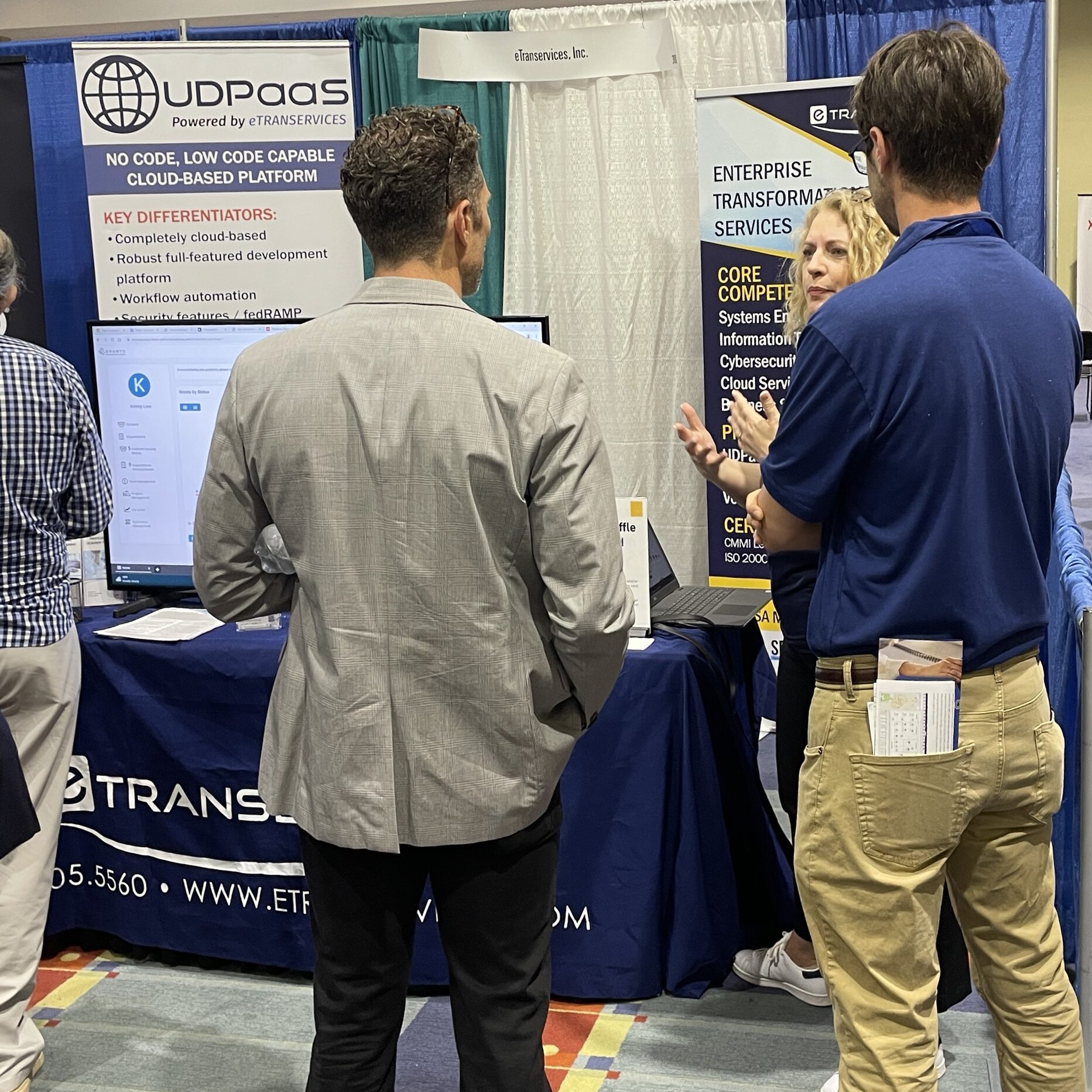 Men at an expo event listening to a booth woman speak